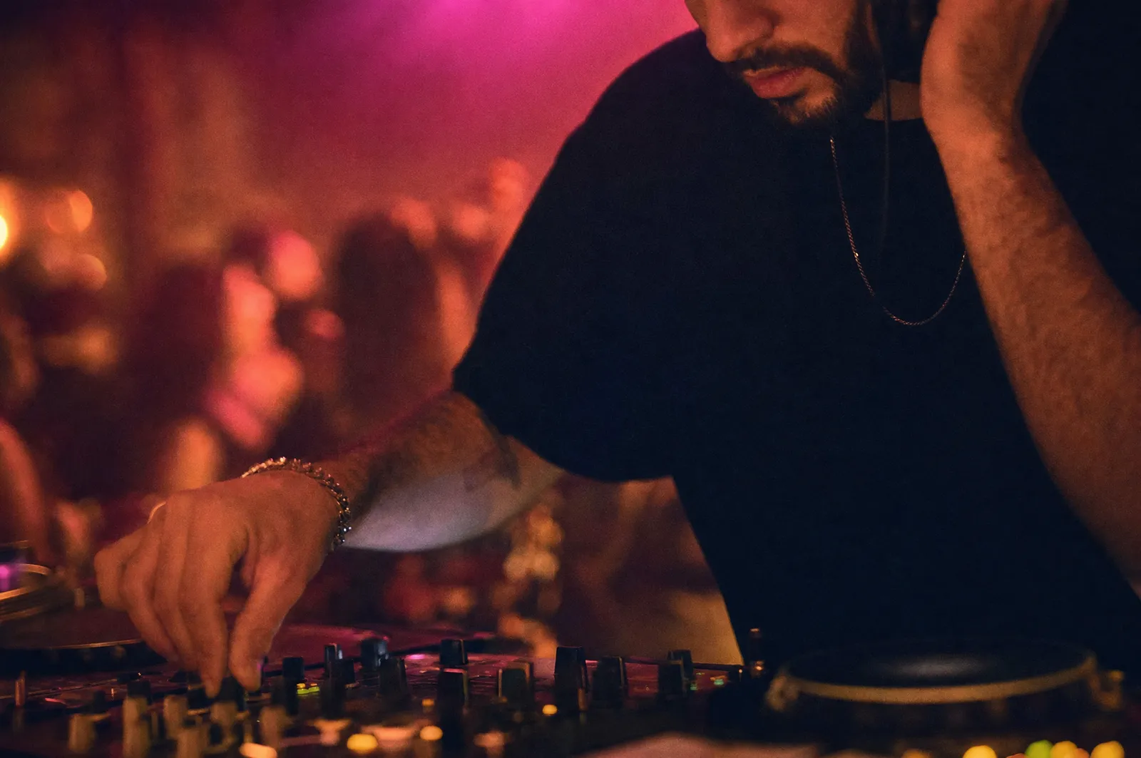 A DJ working the mixer with the dancefloor lit behind them