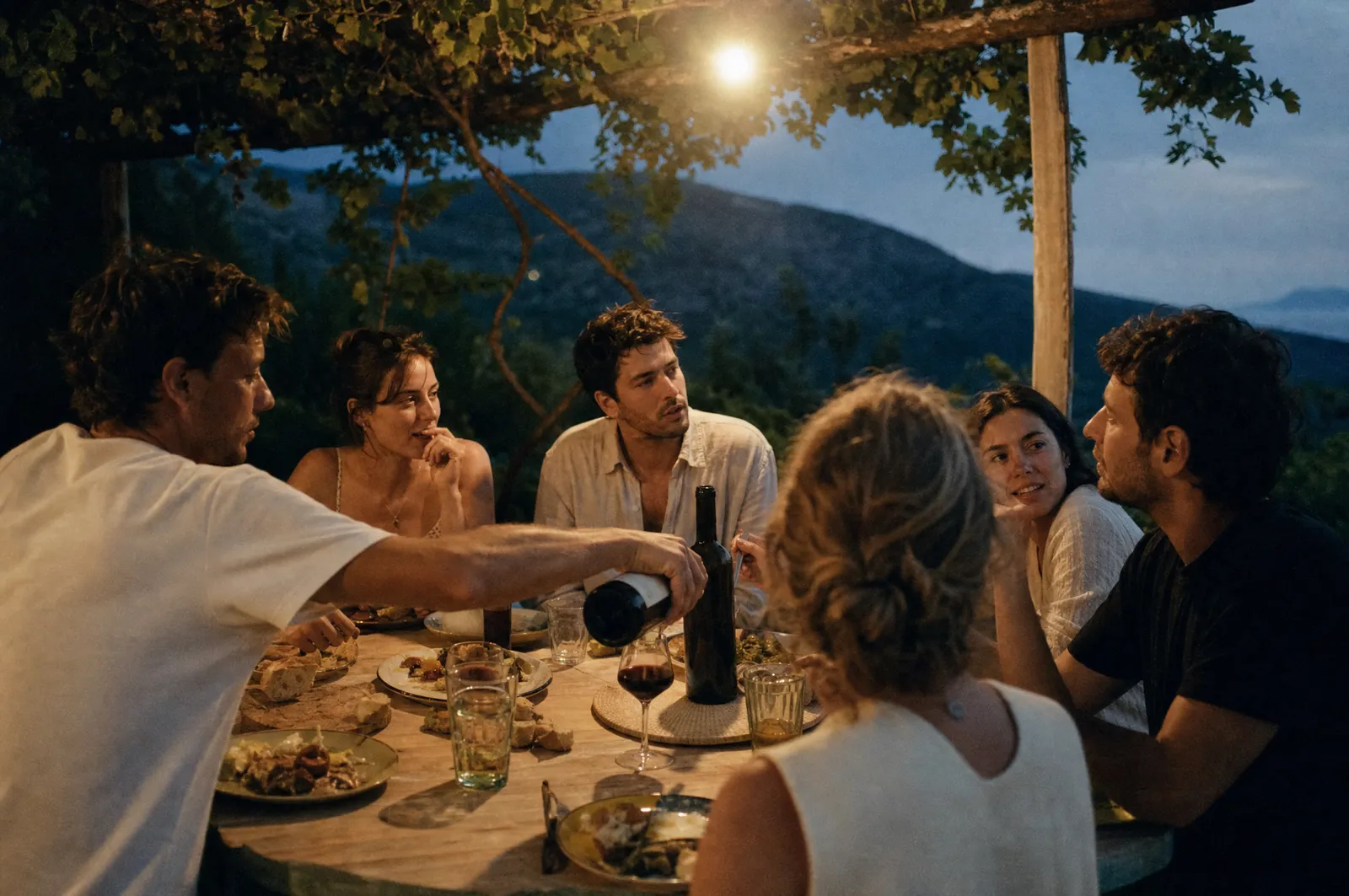 Friends sharing a long dinner on a terrace at dusk while travelling